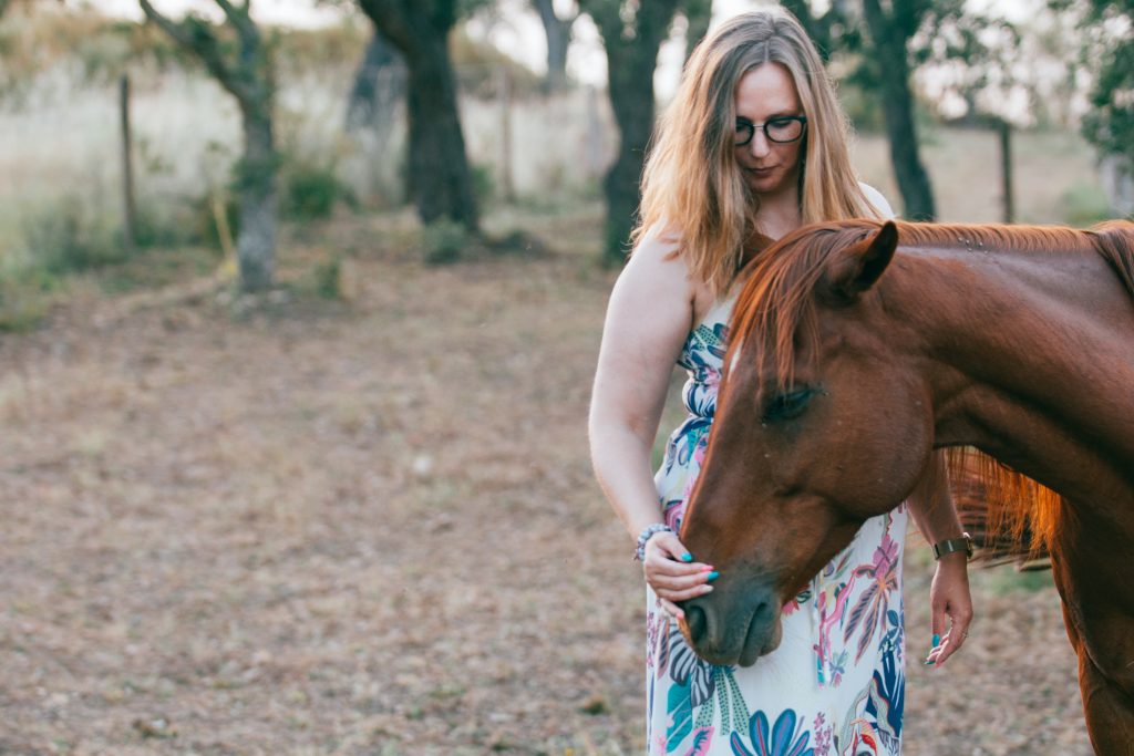 Frau berührt sanft die Nase eines Pferdes im Abendlicht – achtsame Begegnung mit allen Sinnen während eines Retreats in Portugal
