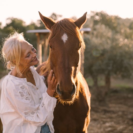 lächelnde Frau in inniger Begegnung mit einem Pferd im Abendlicht. Sinnbild für Therapie mit Pferden in Portugal